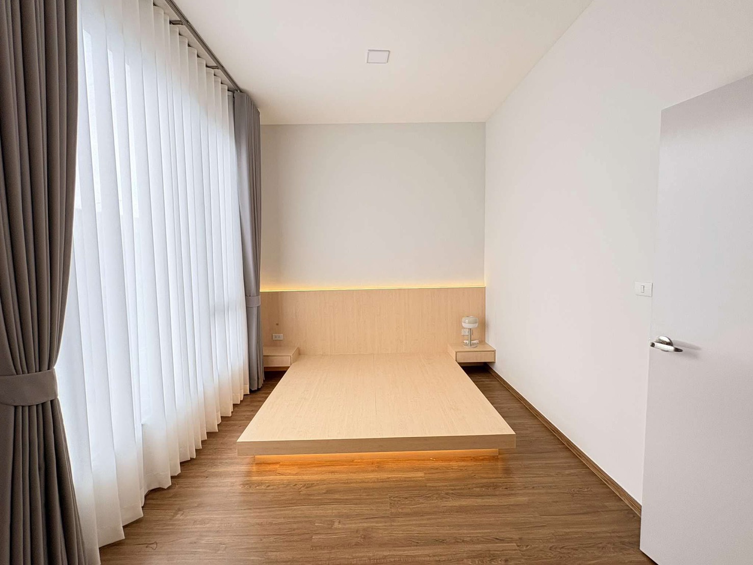 ทาวน์เฮาส์ ให้เช่าในBang Phli, Samut Prakan - ห้องนอนใหญ่พร้อมฐานเตี้ยแบบแพลตฟอร์ม ไฟ LED อุ่นๆ และผ้าม่านสูงจรดเพดาน.