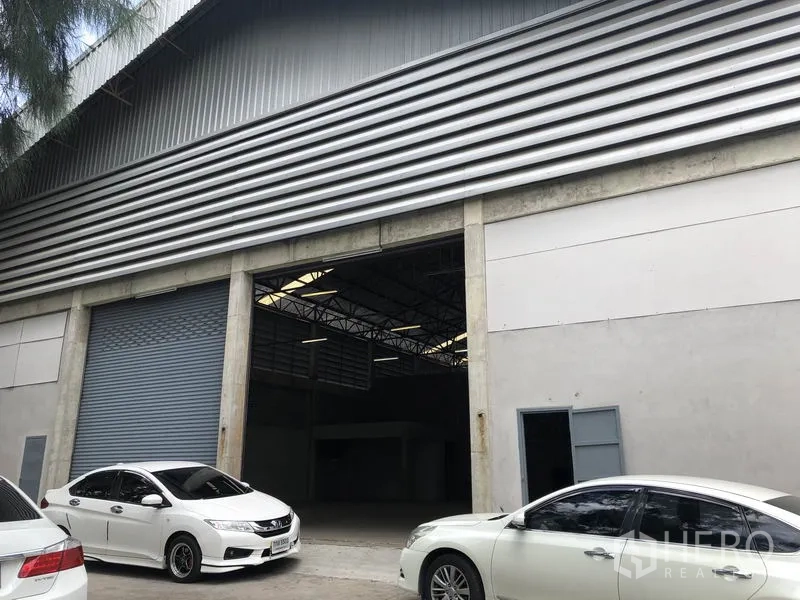 货栈 出租在Khlong Sam Wa, Bangkok - 仓库正面近景，双卷闸门与人行门，前方停车位。