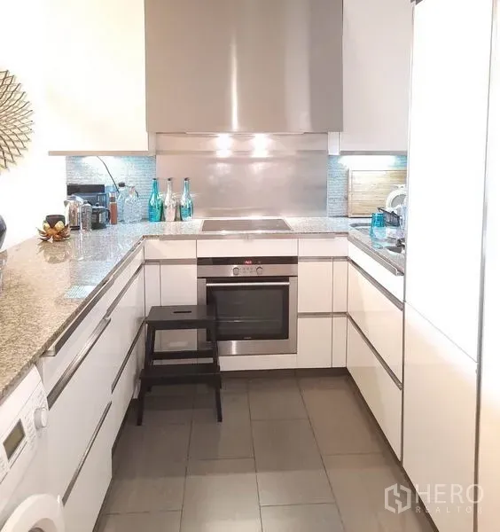 Condominium for rent or sale in Sathon, Bangkok - U‑shaped modern kitchen with white cabinets, granite worktops, a built‑in oven and stainless backsplash.