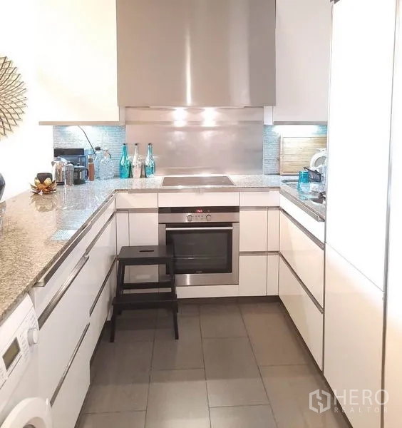 Condominium for rent or sale in Sathon, Bangkok - U‑shaped modern kitchen with white cabinets, granite worktops, a built‑in oven and stainless backsplash.