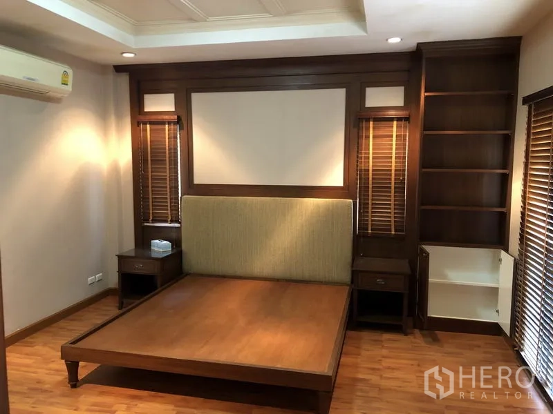独立式住宅 出租或出售在Bang Kapi, Bangkok - 主卧带木质定制床头与开放书架，暖色灯光。