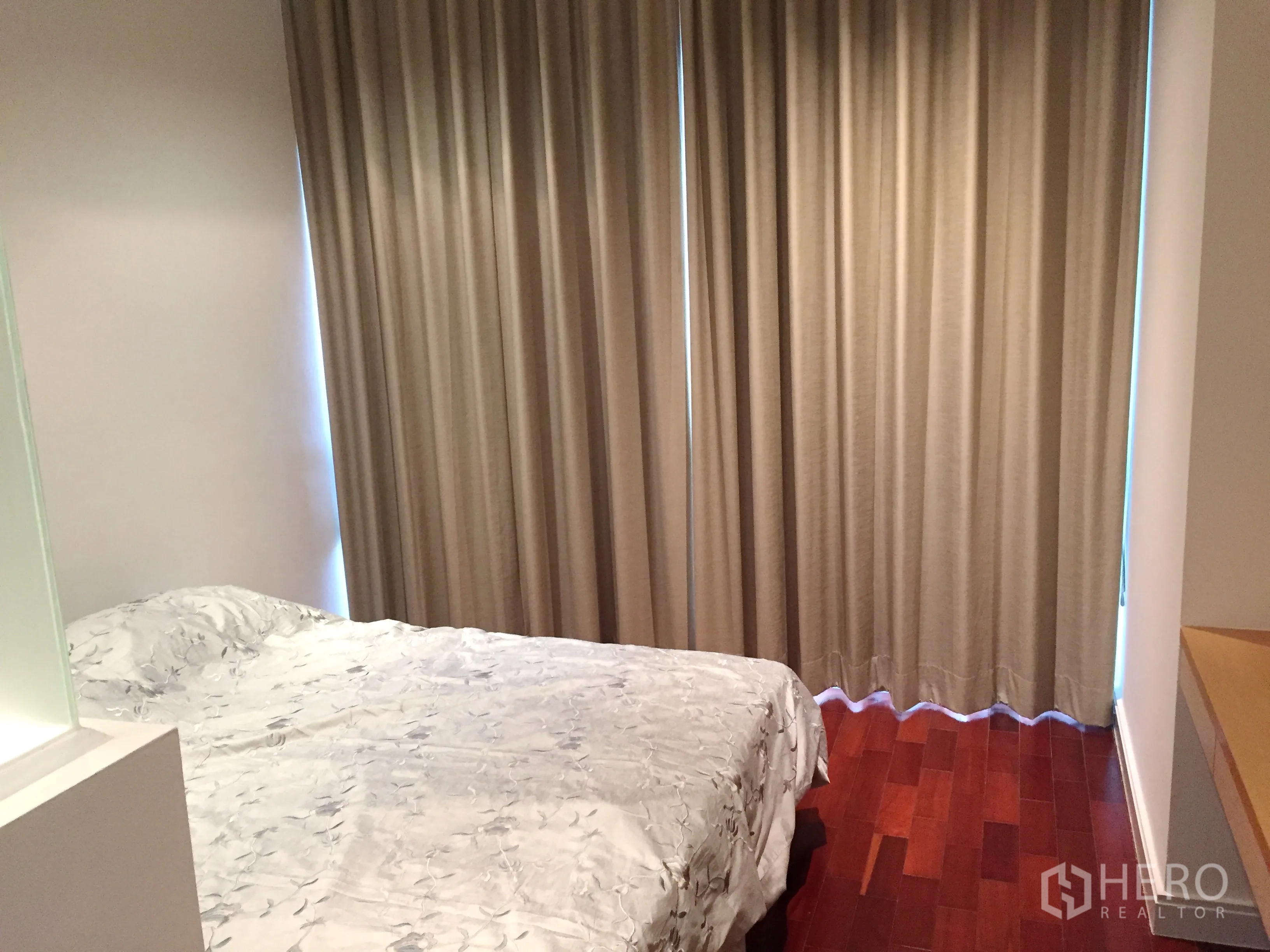 Condominium for rent in Pathum Wan, Bangkok - Cozy bedroom with bedside table, full-length curtains and warm wood floors.