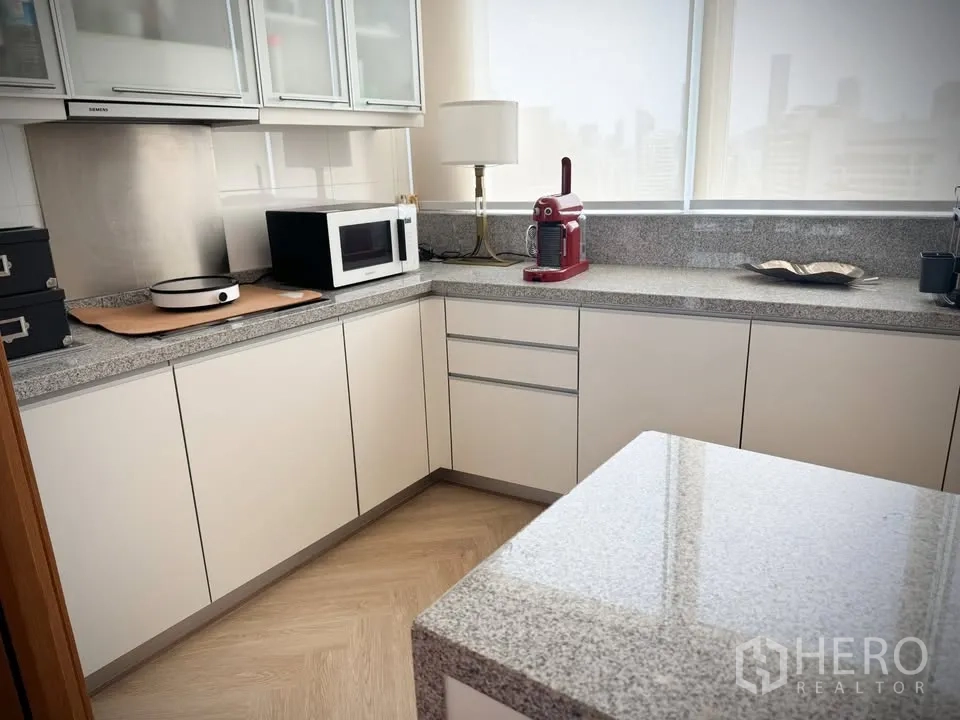 คอนโด for rent or sale in Khlong Toei, Bangkok - ครัวยูเชปสว่าง เคาน์เตอร์หิน ตู้บิลท์อินสีขาว พร้อมไมโครเวฟและเครื่องชงกาแฟสีแดง