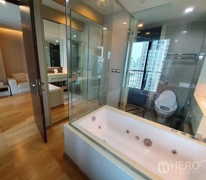 Condominium for sale in Ratchathewi, Bangkok - Bathroom suite with large soaking tub and glass walls, plus separate shower and toilet with city view.