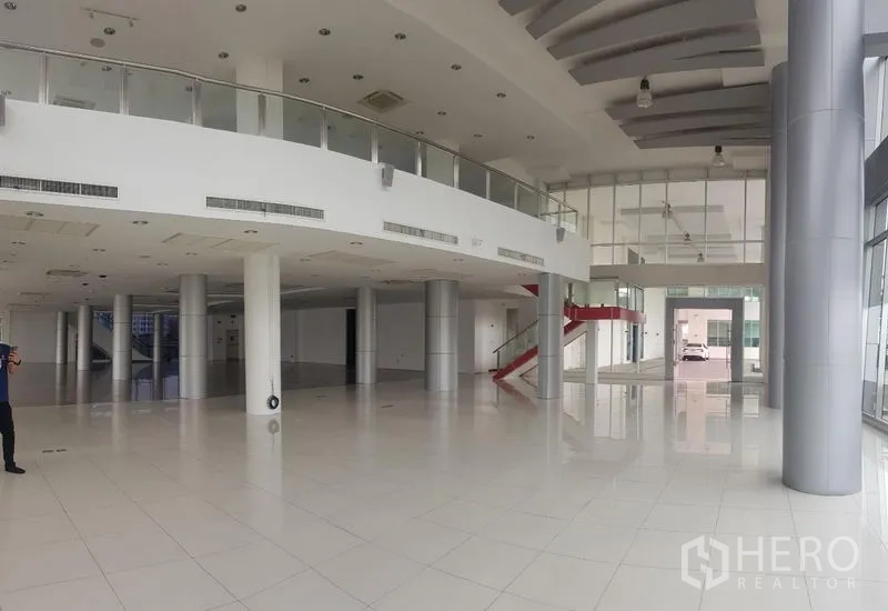 Retail Space for rent in Prawet, Bangkok - Expansive showroom with mezzanine balcony, tall columns, and white tiled floors.