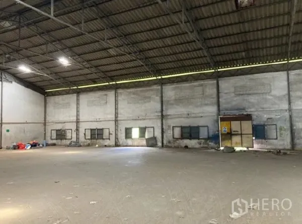 Factory for rent in Samut Prakan - Spacious factory interior with high steel-truss roof, concrete floor, side ventilation windows and a wide loading door.