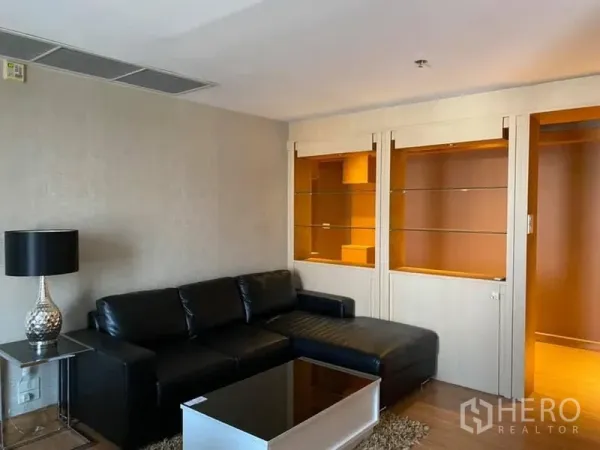 คอนโด ให้เช่าในWatthana, Bangkok - ห้องนั่งเล่นอบอุ่นมีโซฟาหนังเข้ามุม โคมไฟตั้งโต๊ะ และชั้นวางกระจกบิวท์อิน