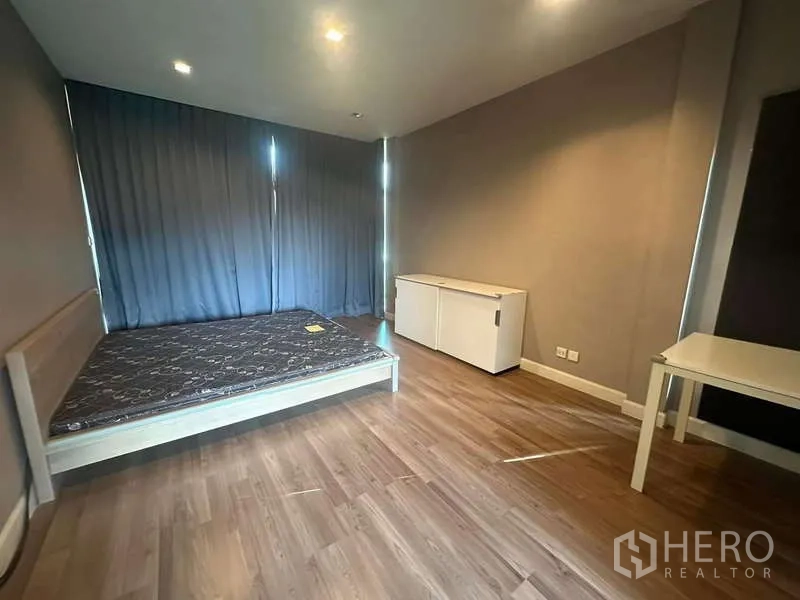 Detached House for rent or sale in Bang Kapi, Bangkok - Spacious bedroom with wood flooring, large bed frame, side cabinet and blackout curtains.