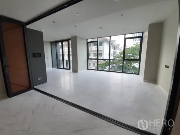 Condominium for rent in Watthana, Bangkok - Bright living area with floor-to-ceiling corner windows and marble-look flooring in a Thonglor condo.