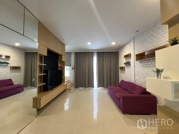 Townhouse for rent in Wang Thonglang, Bangkok - Spacious living room with twin purple sofas, full-height curtains and shelving.