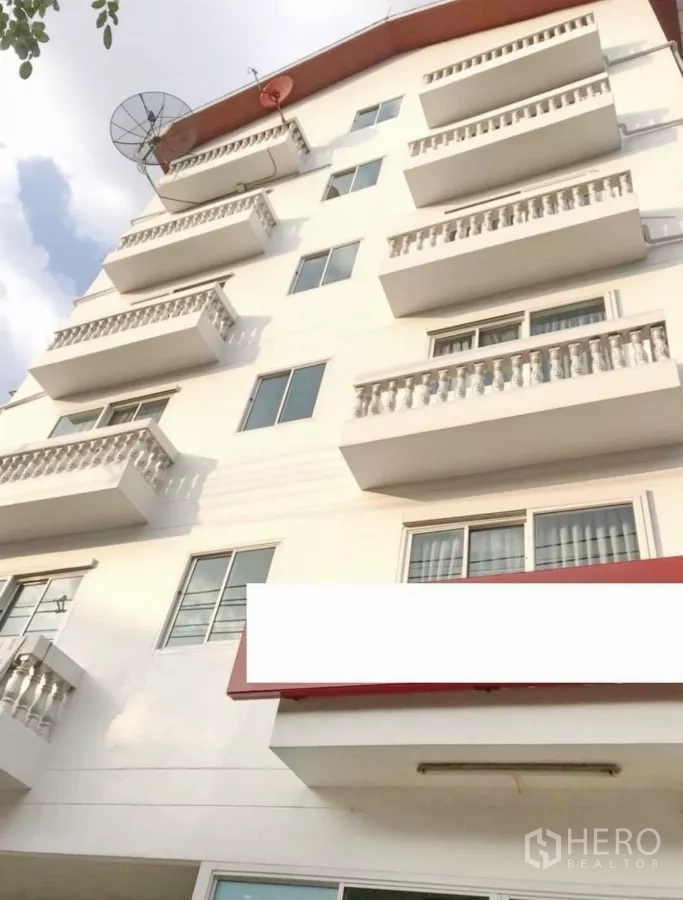 Apartment for sale in Khlong Toei, Bangkok - Multi-storey white apartment exterior with balconies and a satellite dish under clear sky.