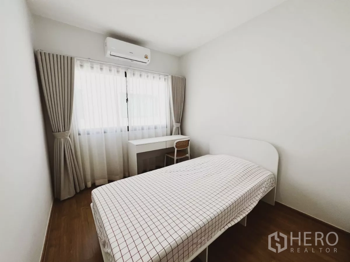 Townhouse for rent in Bang Phli, Samut Prakan - Cozy secondary bedroom with single bed, study desk and air conditioner by a curtained window.