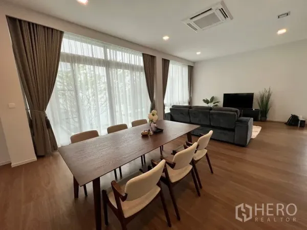 Detached House for rent or sale in Saphan Sung, Bangkok - Open‑plan dining area with six‑seat wooden table adjoining the lounge and large curtains.