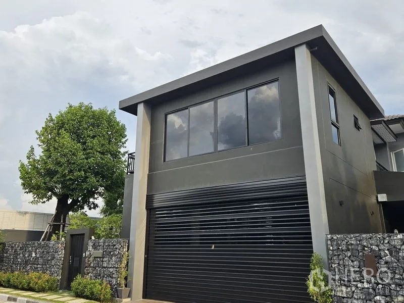 Detached House for sale in Thawi Watthana, Bangkok - Close view of the black roller garage door and upper floor windows of the house.