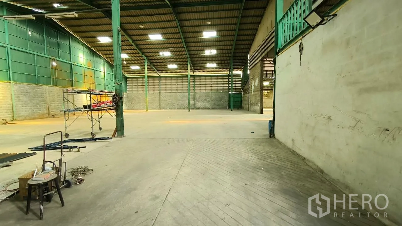 Factory for rent in Mueang Samut Prakan, Samut Prakan - Interior view from a loading area with scaffolding and illuminated roof panels.