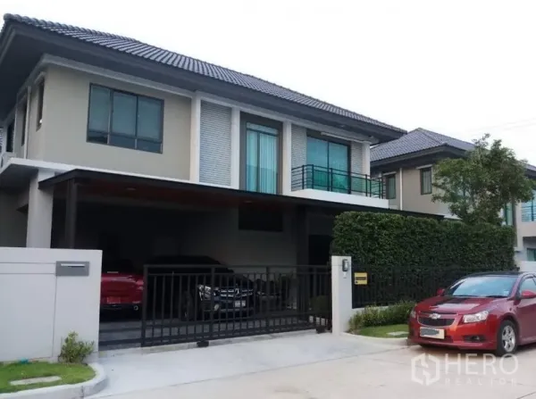 独立式住宅 出售在Nonthaburi - 现代两层独栋别墅外观，带电动大门车棚与阳台，绿篱整齐。