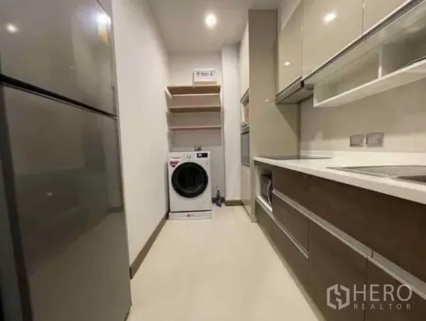 Condominium for rent in Watthana, Bangkok - Galley kitchen with glossy cabinets, refrigerator and in-unit washer with shelving.