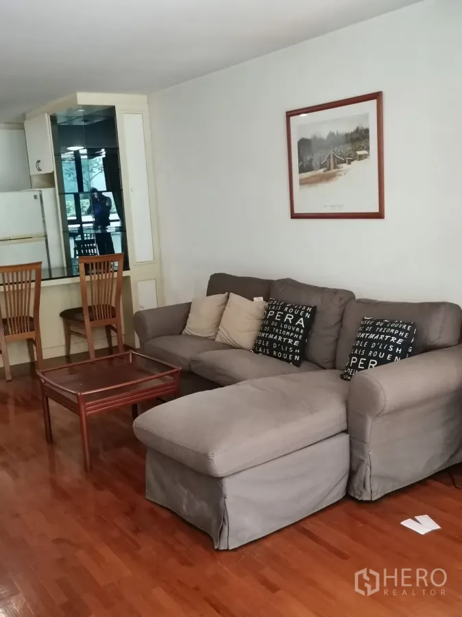 คอนโด ให้เช่าในPathum Wan, Bangkok - ห้องนั่งเล่นแบบโอเพนพร้อมโซฟาตัวแอลสีเทา โต๊ะกลาง และพื้นไม้เงา ข้างตู้กระจกบานใหญ่