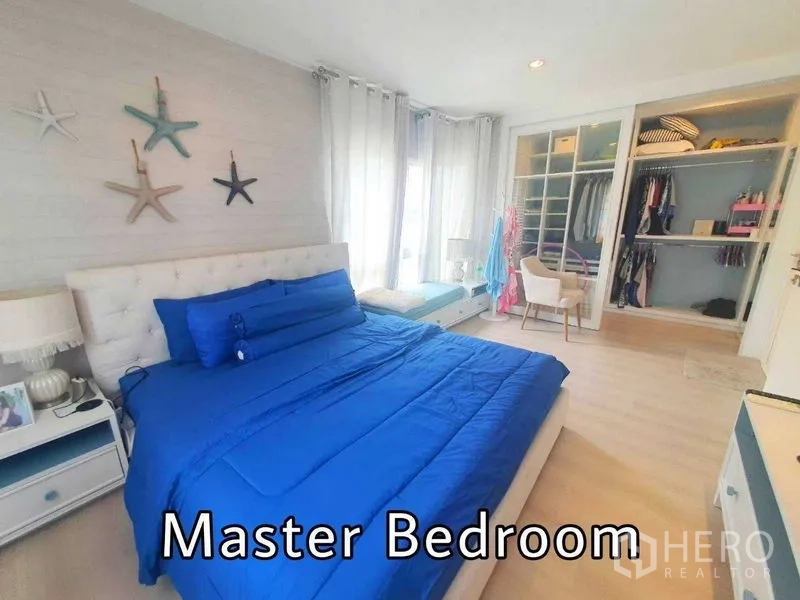 Detached House for sale in Samut Prakan - Bright master bedroom with blue bedding, large windows, and built-in wardrobe.