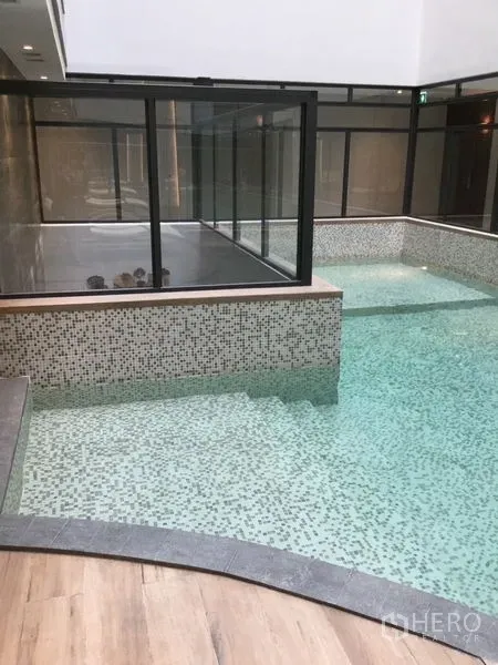 Condominium for rent in Watthana, Bangkok - Indoor mosaic-tiled swimming pool with glass enclosure and wooden deck edge.