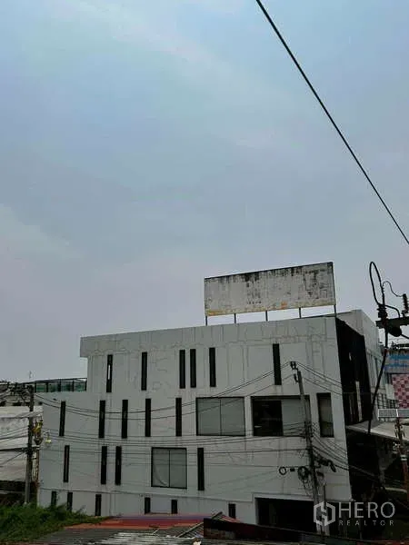 Home Office for rent or sale in Bang Phli, Samut Prakan - Side and rear view of the contemporary building with vertical windows and rooftop billboard structure.