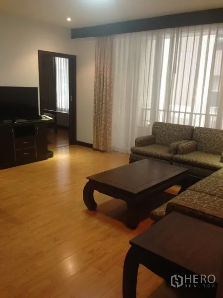 Condominium for rent in Pathum Wan, Bangkok - Bright living room with wood floors, patterned sofa set, coffee table, TV console and sheer curtains.