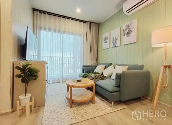 Condominium for rent or sale - Living area with balcony access, sheer curtains, wall-mounted TV and green feature wall.