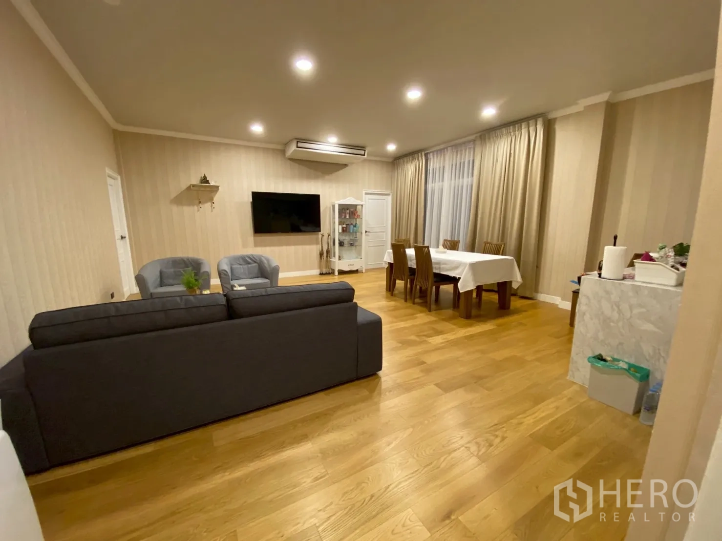 Detached House for sale in Mueang Nakhon Pathom, Nakhon Pathom - Warm living and dining area with wood floors, sofa set, wall-mounted TV and large curtains.