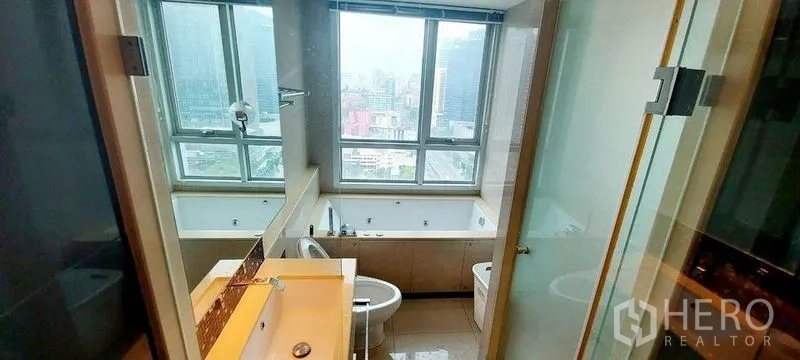 Condominium for rent in Ratchathewi, Bangkok - Bathroom with a bathtub beside a large window overlooking the city skyline.