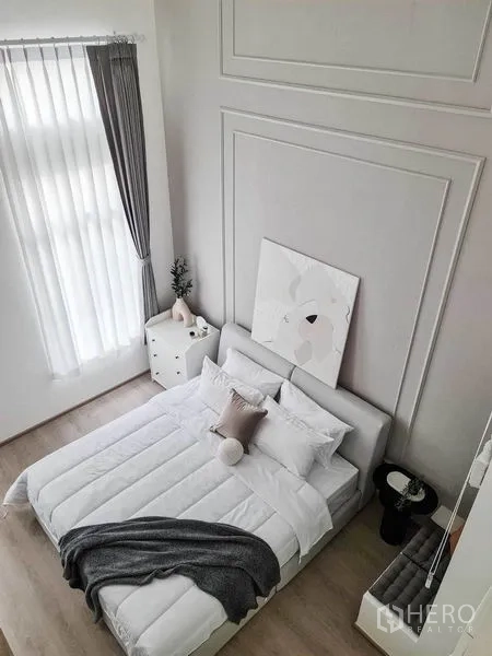 联排别墅 出租在Prawet, Bangkok - 俯视极简卧室，层次墙饰与高挑窗帘相映成趣。