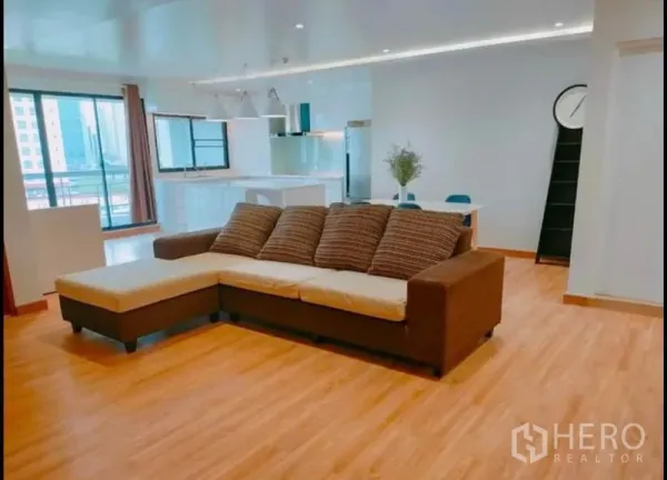 公寓 出售在Watthana, Bangkok - 采光充足的开放式客厅，L形沙发、木地板和阳台移门。