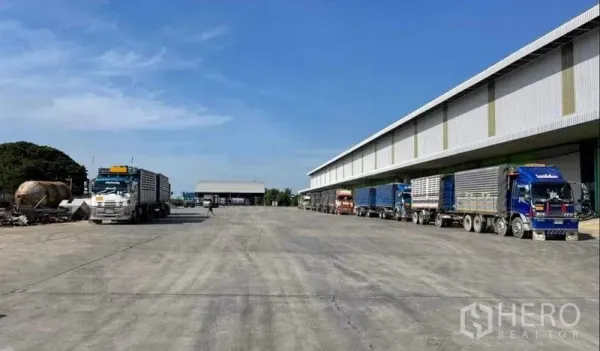 工厂 出租在Sai Noi, Nonthaburi - 宽阔的混凝土装卸场，多辆货车停靠在带雨棚的装卸月台旁。