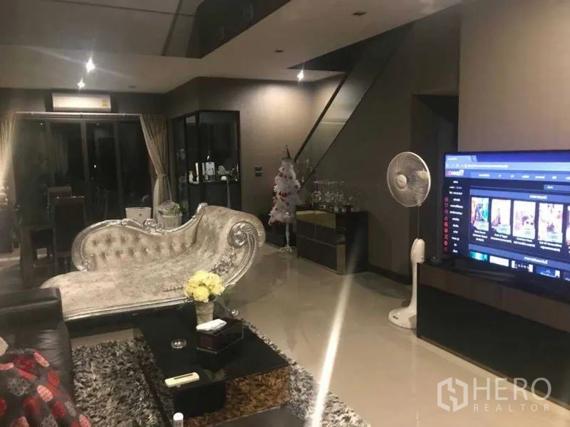 ทาวน์เฮาส์ ให้เช่า - ห้องรับแขกกว้างตอนกลางคืน ทีวีจอใหญ่ มุมทานอาหาร และบันไดราวกระจก