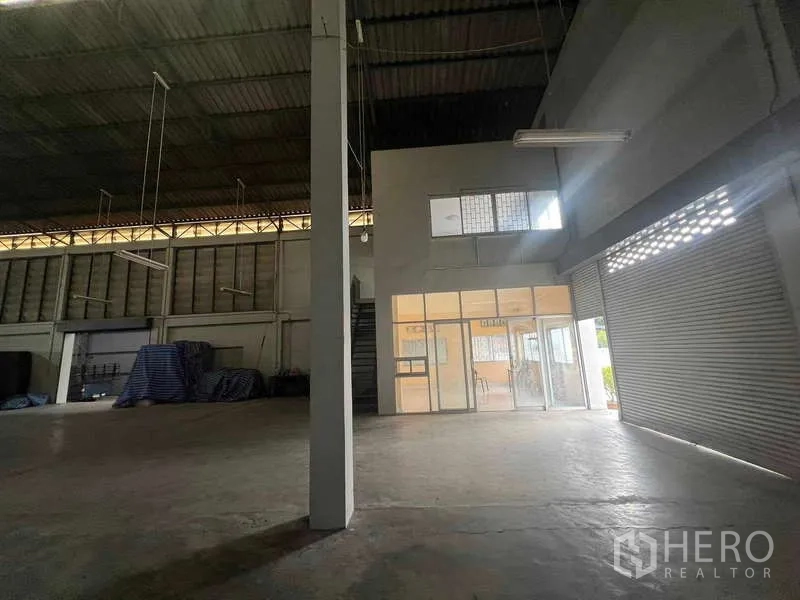 Warehouse for rent in Lam Luk Ka, Pathum Thani - Warehouse interior showing a mezzanine office box, roller shutter, and open floor area.
