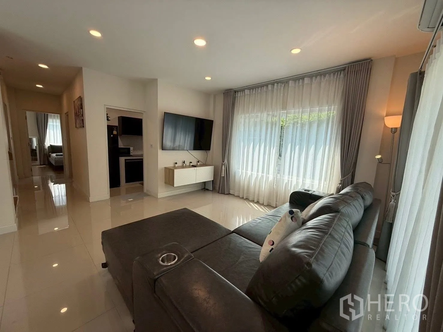 Detached House for rent in Prawet, Bangkok - Bright living room with a large sectional sofa, mounted TV and sheer curtains.