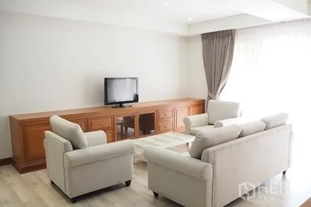 Condominium for rent in Pathum Wan, Bangkok - Cozy lounge with TV on a long wooden console and two armchairs.