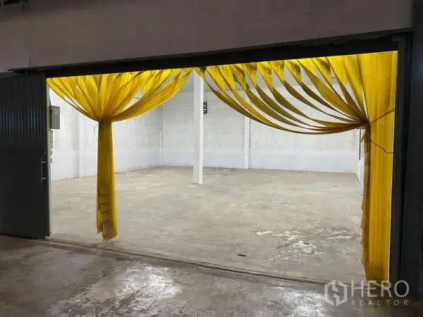Warehouse for rent in Chatuchak, Bangkok - Wide entry with yellow PVC strip curtains opening into a concrete-floor warehouse.