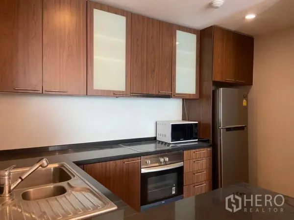 公寓 出租在Sathon, Bangkok - 现代厨房，木质柜体、石材台面，内置烤箱、微波炉与不锈钢冰箱。