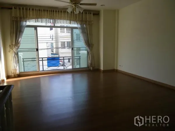 带办公室的家 出租或出售在Suan Luang, Bangkok - 宽敞起居区，木地板、吊扇，大幅推拉窗通向阳台。