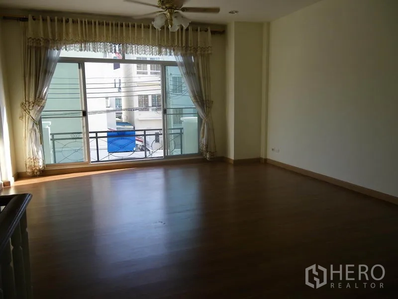 带办公室的家 出租或出售在Suan Luang, Bangkok - 宽敞起居区，木地板、吊扇，大幅推拉窗通向阳台。