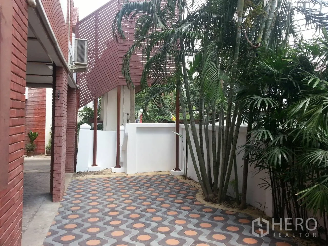 Townhouse for rent or sale in Watthana, Bangkok - Shaded patio with patterned tiles, palm trees and red-brick exterior walls.