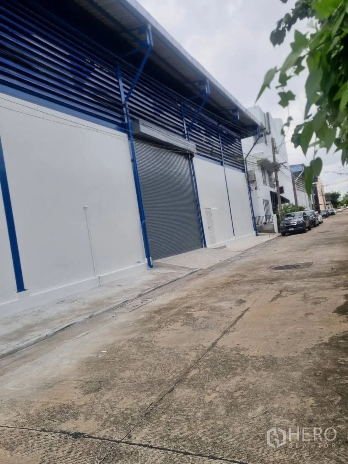 Warehouse for rent in Thepharak, Nakhon Ratchasima - Street view of the warehouse facade with roller shutters and parking lane.