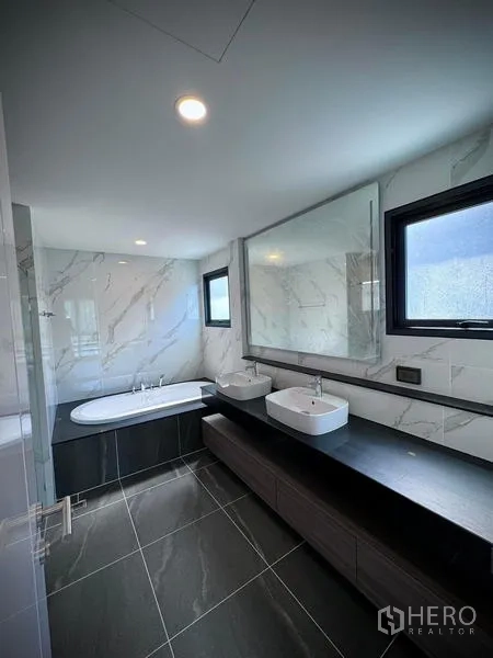 Detached House for rent or sale in Bang Phli, Samut Prakan - Modern bathroom with double sinks, large mirror, marble-tiled walls, and a built-in bathtub.