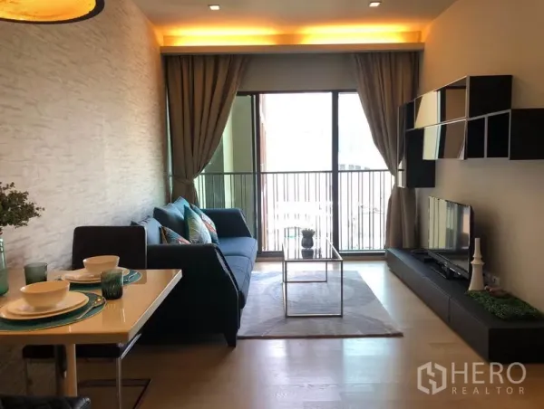 คอนโด ให้เช่าในBangkok - พื้นที่นั่งเล่น–รับประทานอาหารสว่างไสว ประตูกระจกสูงจรดเพดานออกสู่ระเบียง พร้อมชั้นวางผนังและชุดโต๊ะอาหาร