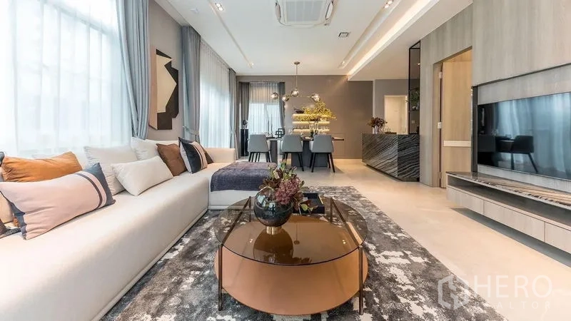 Detached House for rent in Prawet, Bangkok - Living room with long sofa, round coffee table and built-in TV wall.
