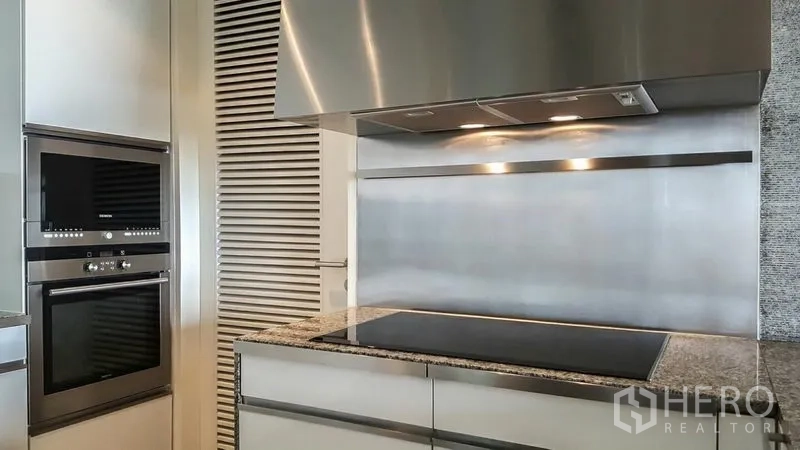 Condominium for rent or sale in Sathon, Bangkok - Contemporary kitchen featuring an induction cooktop, stainless range hood, and built-in ovens.