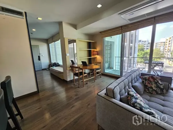 Condominium for sale in Phra Khanong, Bangkok - Open-plan lounge with work desk and shelving beside floor-to-ceiling windows.