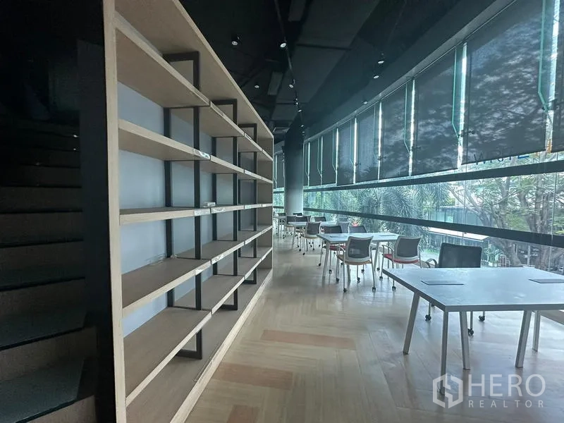 Office Space for rent - Long workspace with wall-length shelving and desks lined along panoramic windows with roller blinds.