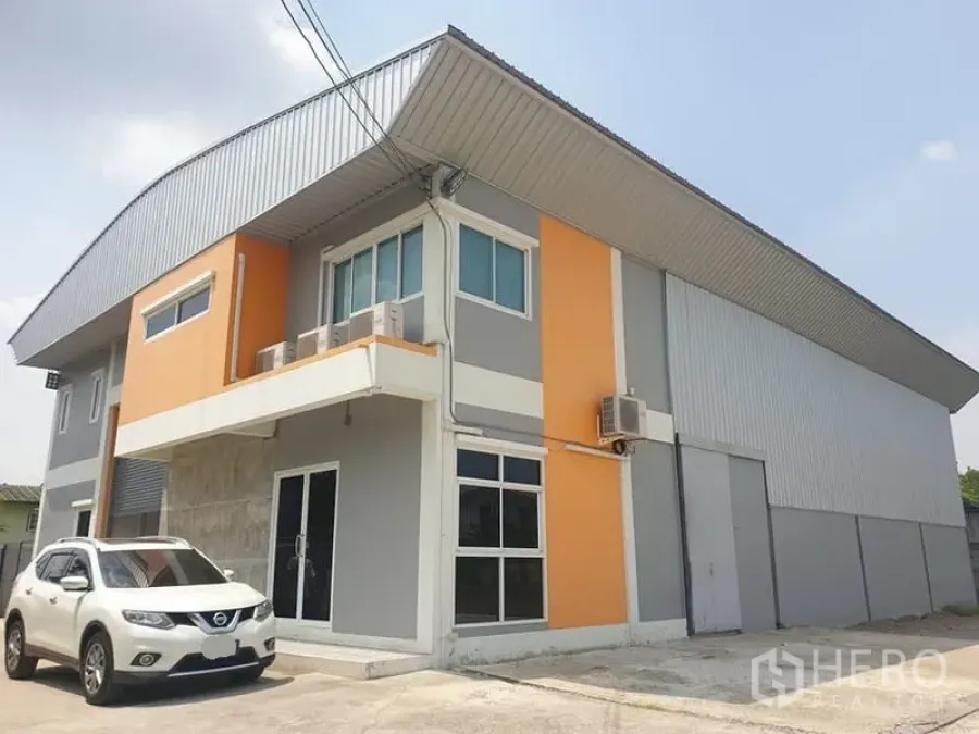 Warehouse for rent in Bang Kapi, Bangkok - Modern two-storey warehouse exterior in Bang Kapi with orange-grey facade, parking and a high roller shutter.
