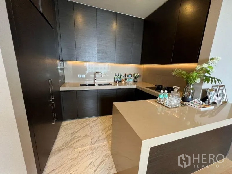 公寓 出租在Bang Rak, Bangkok - 现代U型厨房，深色橱柜、石英台面与橱柜下照明。